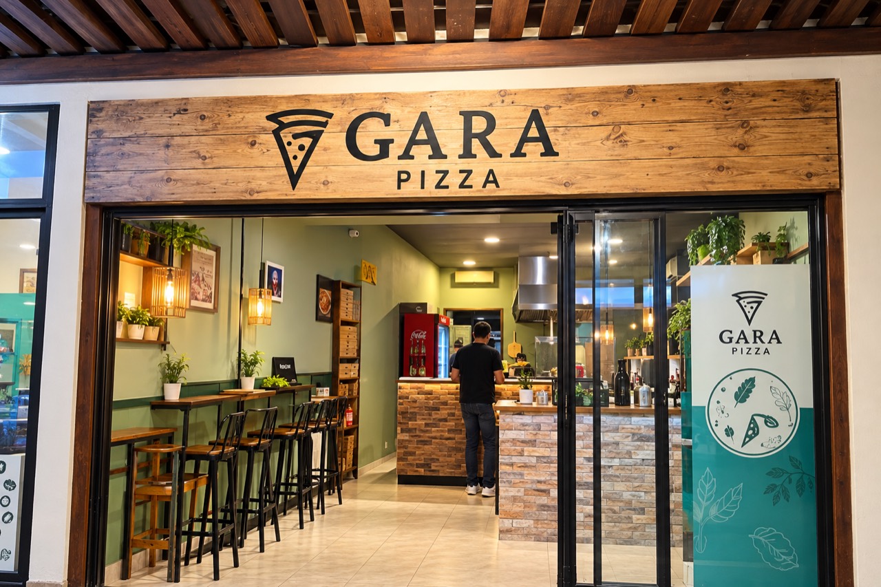 Fachada real da Gara Pizza, com letreiro de madeira, iluminação acolhedora e mesas junto à entrada.